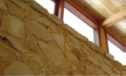 Una foto del interior de una casa que usa piedras para una pared, que son duraderas y de bajo mantenimiento. Hay ventanas en la parte superior de la pared y un techo de madera.