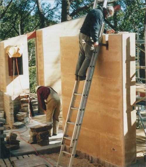 Ein Foto von zwei Arbeitern, die eine Stampflehmwand errichten.