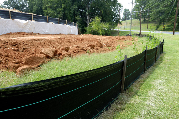 A temporary, permeable barrier of geo-textile is installed in a trench and supported by wooden posts. 