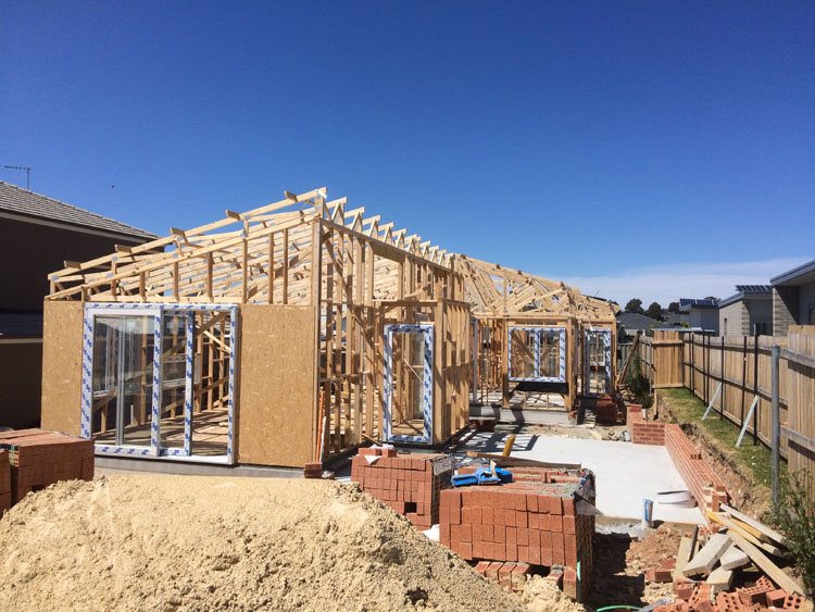 A building site with a house in its early stages of construction. There is a concrete slab, timber faming and some glass sliding doors installed.