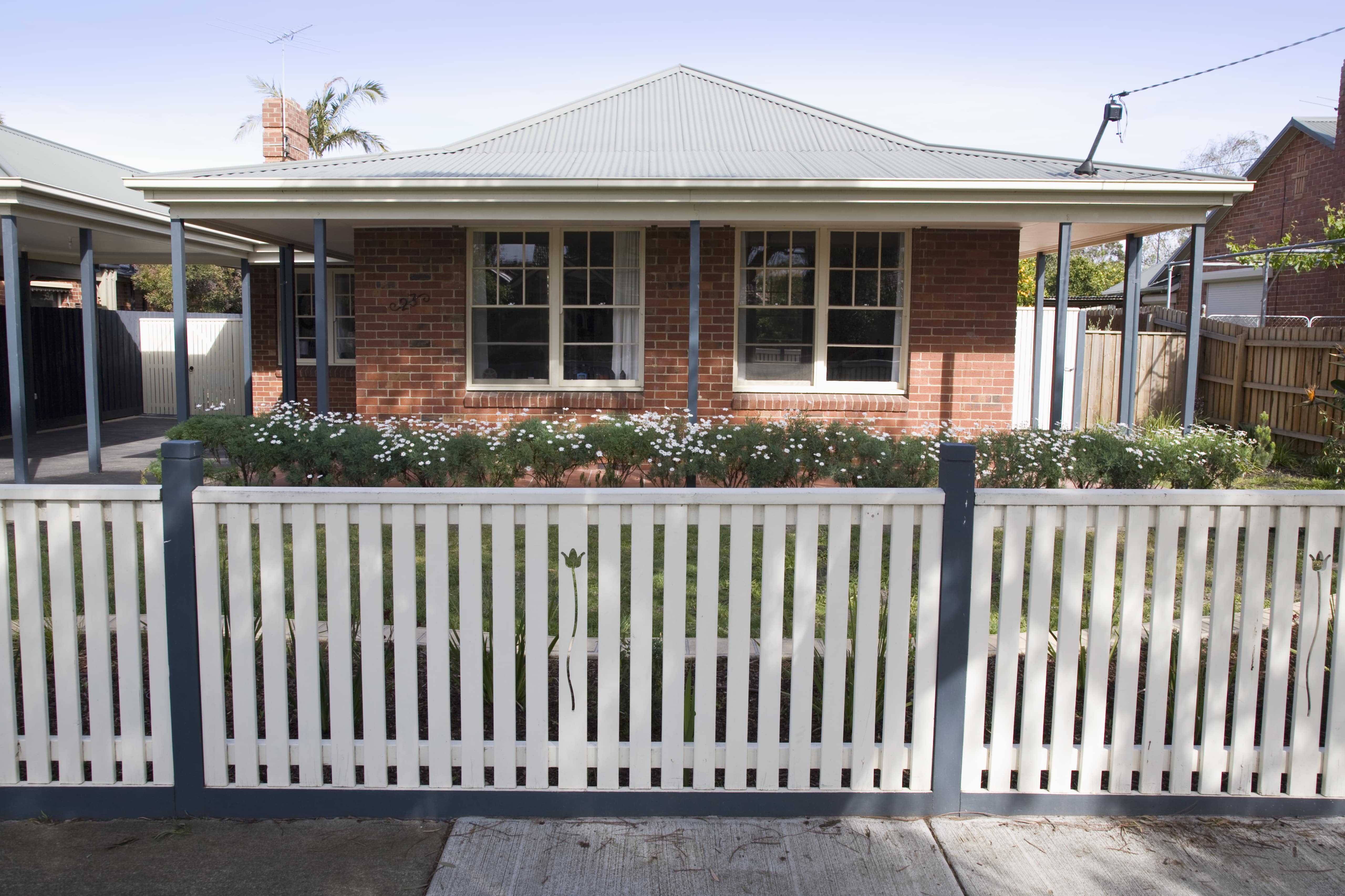 An example of a white picket fence made from steel, with spaces between the bars to allow persons on the street to see the house and yard.