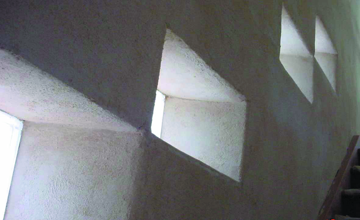 A photo of an interior wall constructed from autoclaved aerated concrete. It has some square holes cut out as windows, and follows up a staircase.