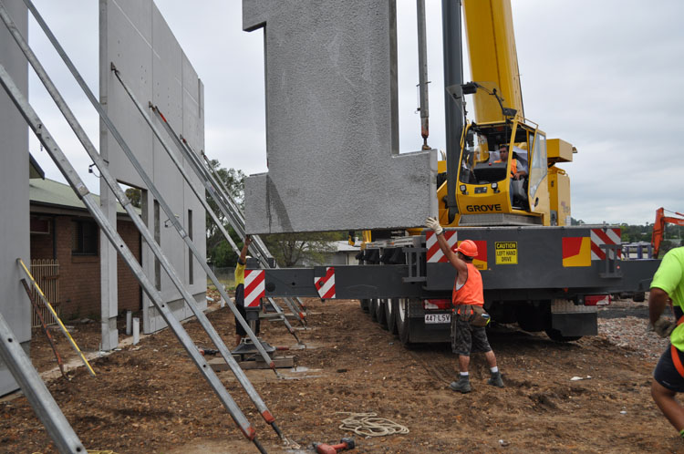 A photo of a crane lifting precast walls into place. Workers are helping to guide the walls into place.