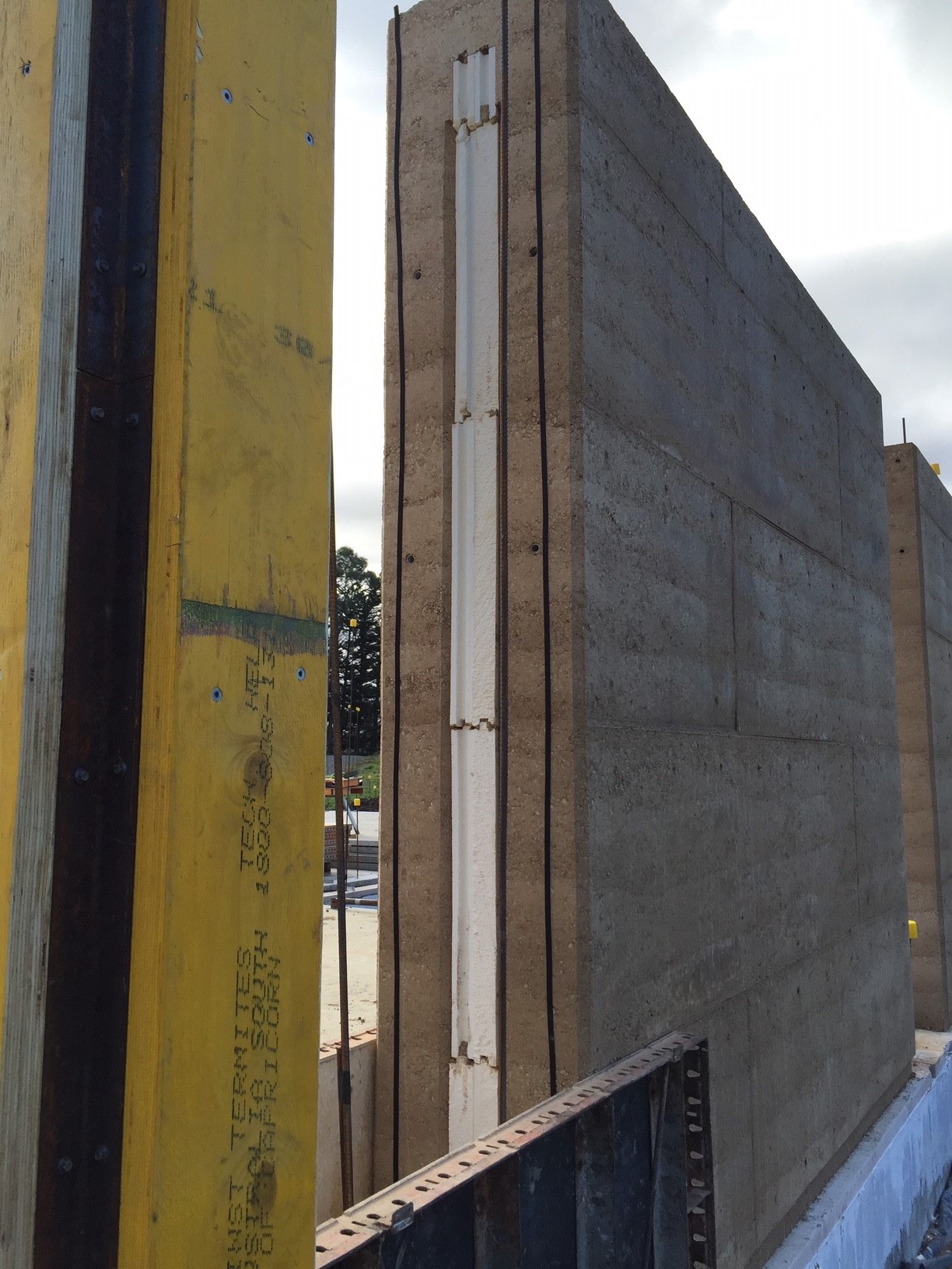 A wall of rammed earth compressed in lifts with an insulation layer centred sitting atop a concrete foundation.  