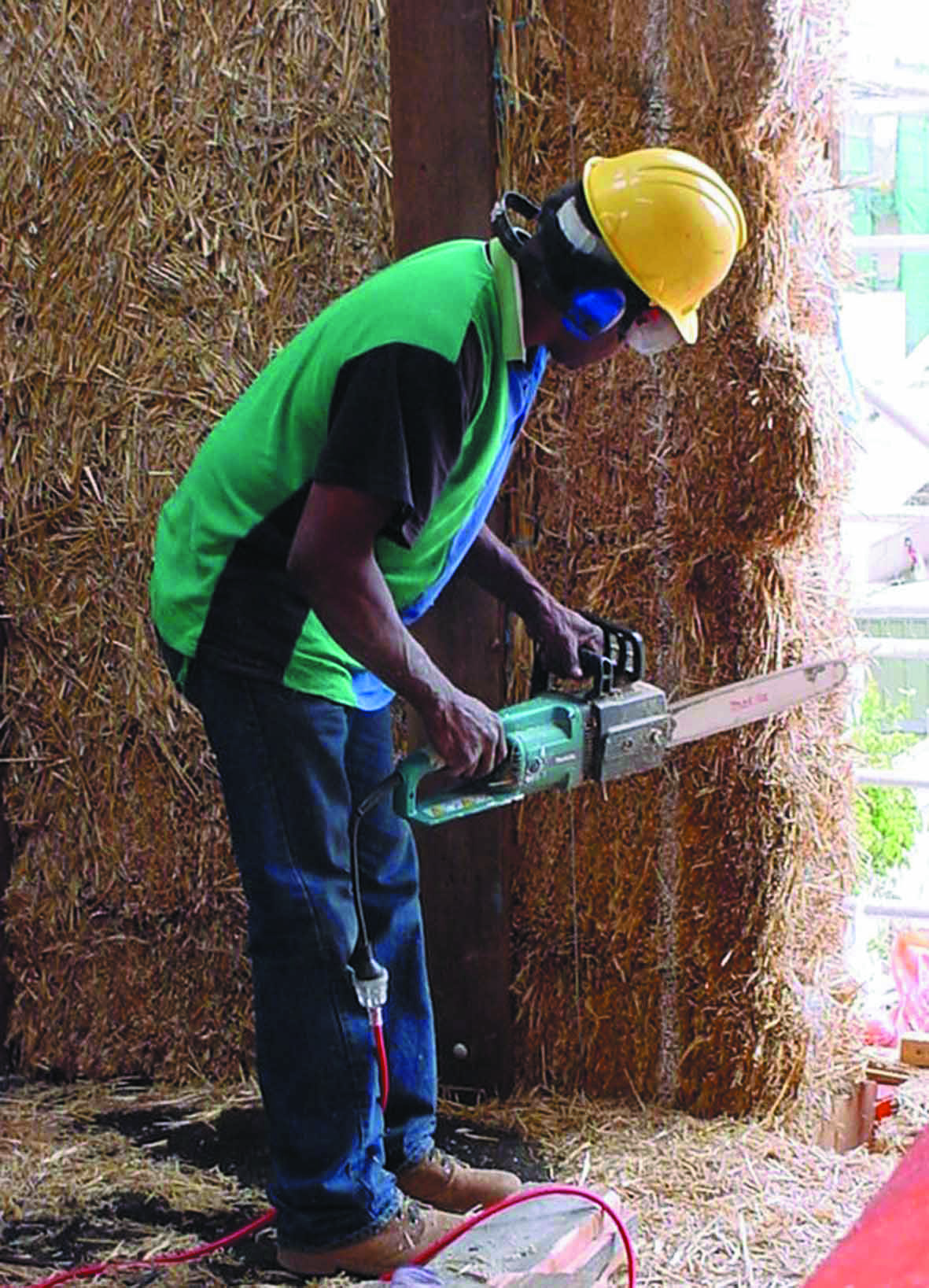 A photo of a worker using a chain saw to trim placed straw bales.