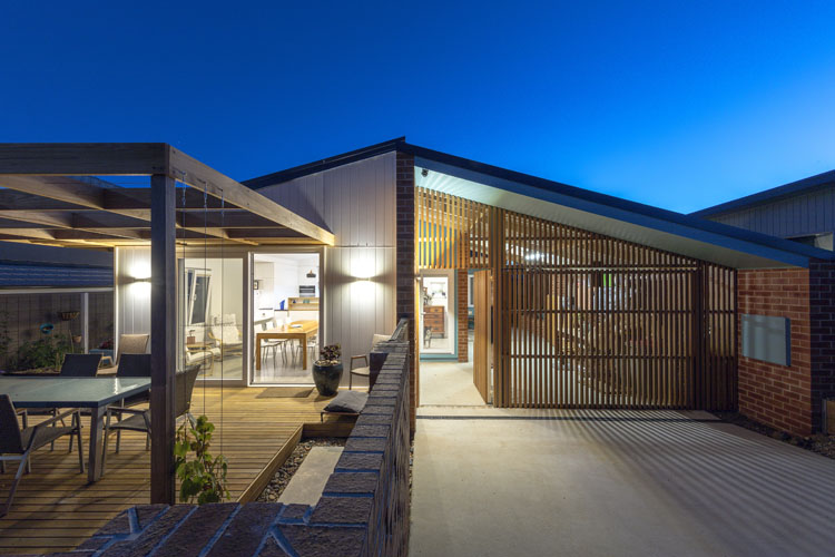 A Canberra home photographed at dusk. It features an A-frame roof, a large outdoor timber deck and a carport. 